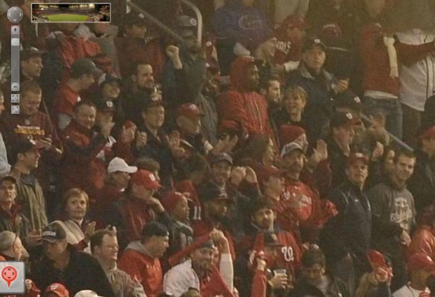 Eine Menge Menschen mit Gegenständen in den Händen, animierte Logos oben links und unten links sowie ein Stadionbild oben.