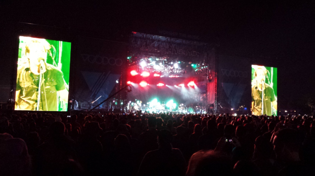 Eine Konzertszene mit einer Menge unten, ein großes Display links und ein weiteres Display rechts.