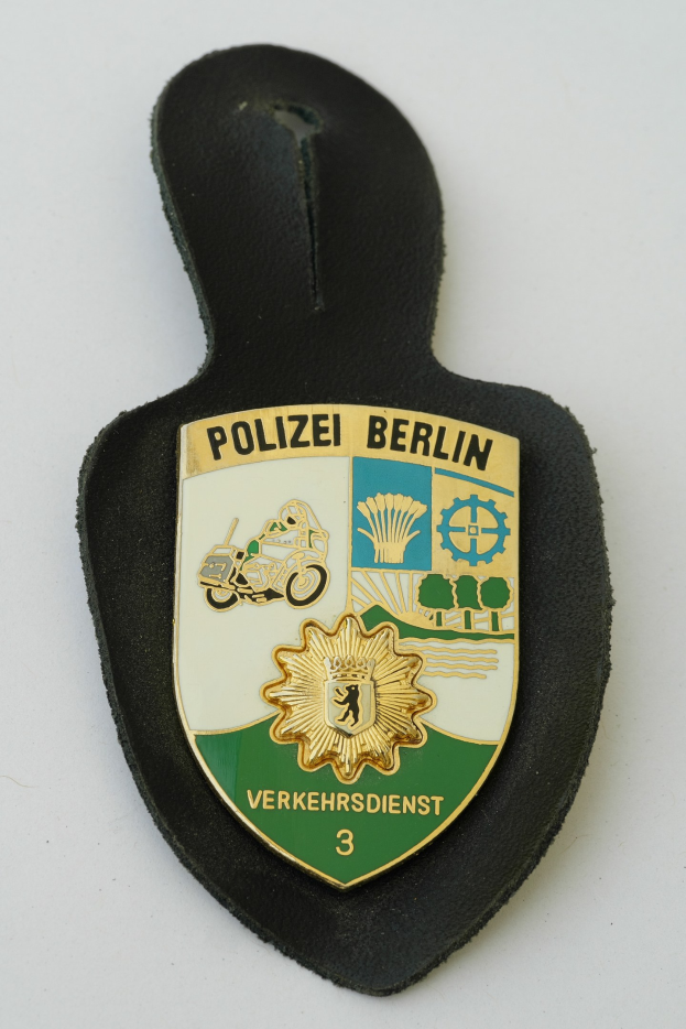Ein schildförmiges Polizeibadge mit der Aufschrift 'Polizei Berlin' auf einem blauen Hintergrund, einem weißen Rand und einem zentralen weißen Stern, das auf einer Oberfläche liegt.