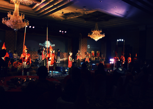 Eine Gruppe von Menschen, die eine Vorstellung ansehen, mit zwei Kronleuchtern an der Decke.