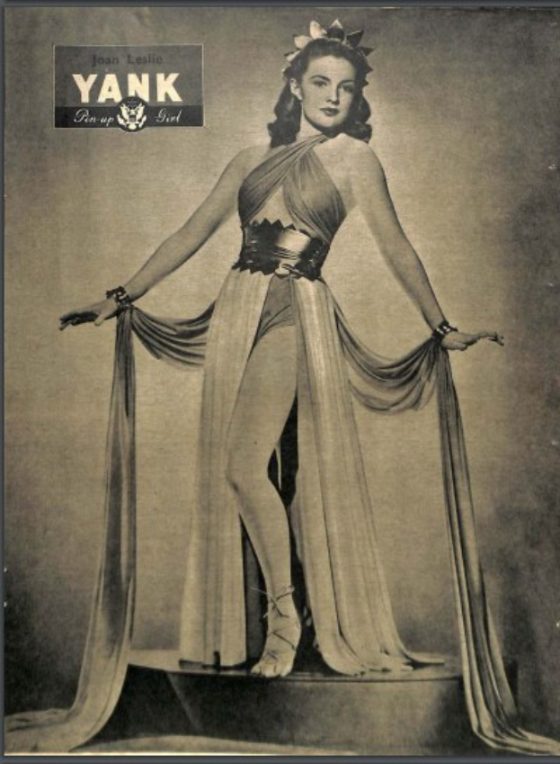 Ein Schwarz-Weiß-Foto von Schauspielerin Joan Leslie, die auf einer Bühne steht und ein langärmliges, hochgeschlossenes Kleid mit einer 1940er-Jahre-Frisur und dezentem Make-up trägt, die Augen geschlossen in einer friedlichen Pose.