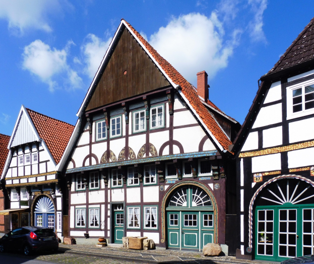 Eine Reihe von Fachwerkhäusern in Heidelbergs Altstadt, mit Fahrzeugen auf der Straße davor und einem bewölkten Himmel dahinter.