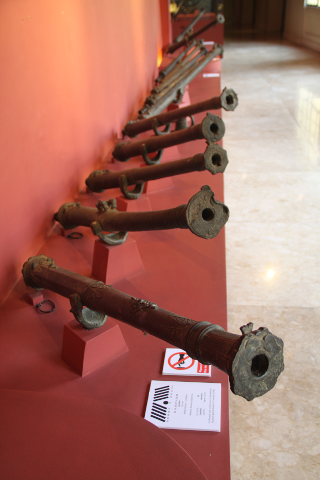 Eine Reihe von Kanonen in einem Museum ausgestellt, mit Papieren drumherum, gegen eine Wand und über einen Boden.