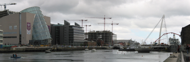 Ein Fluss mit Schiffen, eine Brücke, Gebäude, Baukräne und der Himmel im Hintergrund.