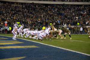 Ein Fußballspiel im Gange mit Spielern in Sportkleidung und Helmen auf dem Boden, Tribünen und Beschriftungen im Hintergrund.