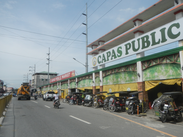 Eine belebte Stadtstraße mit Fahrzeugen, Gebäuden und einigen Menschen, mit einem Schild, auf dem "Capas Public" steht.