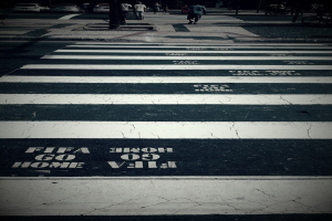 Menschen überqueren eine Fußgängerfurt, während Autos in der oberen linken Ecke zu sehen sind.