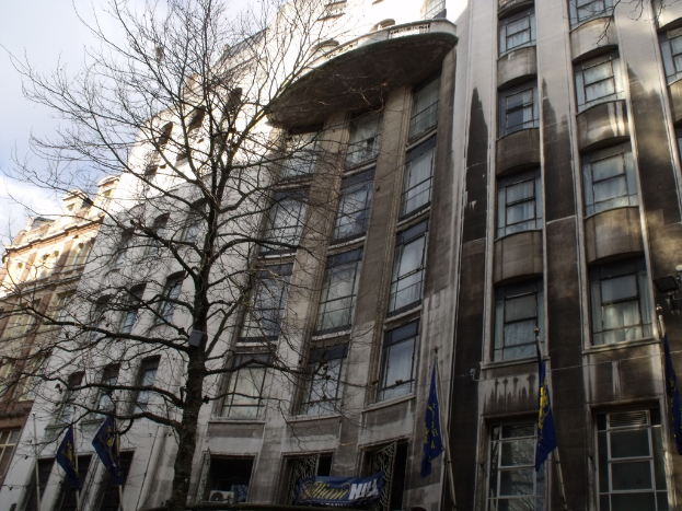Gebäude mit Fenstern, einer Fahne und Fahnen an Stangen unten und einem Baum mit Zweigen.