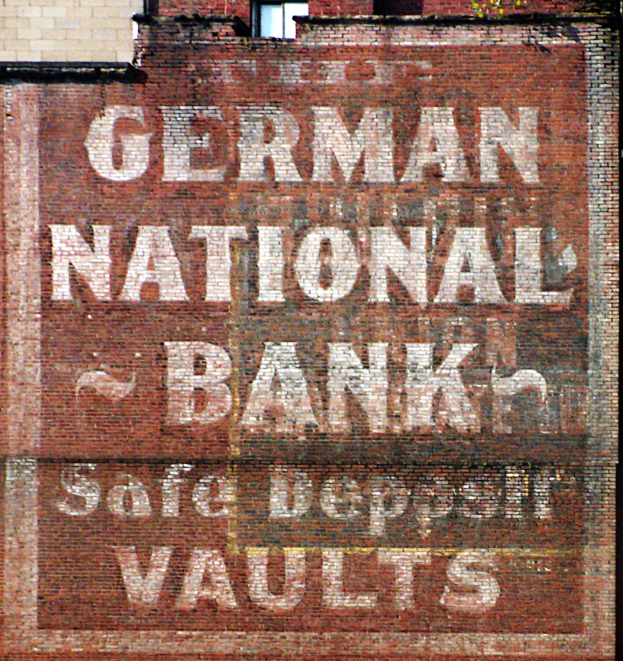 Eine Ziegelwand mit einem Schild, auf dem "Deutsche Nationalbank Safe Deposit Vaults" steht und ein Fenster oben.