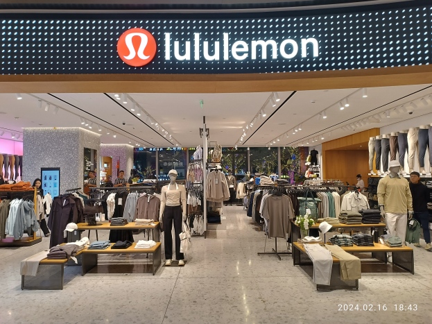 Das Innere eines lululemon-Ladens in Singapur mit Schaufensterpuppen in der neuesten Mode, Kleidung an Bügeln, Tischen mit verschiedenen Artikeln, Deckenleuchten und einem Namensschild mit Text sowie einem Wasserzeichen auf dem Bild.