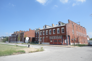 Ein Gebäude mit Masten und Straßenlaternen, umgeben von Bäumen und Fahrzeugen auf beiden Seiten, mit einem Weg, Gras und einem Feuerlöscher unten und Himmel oben.
