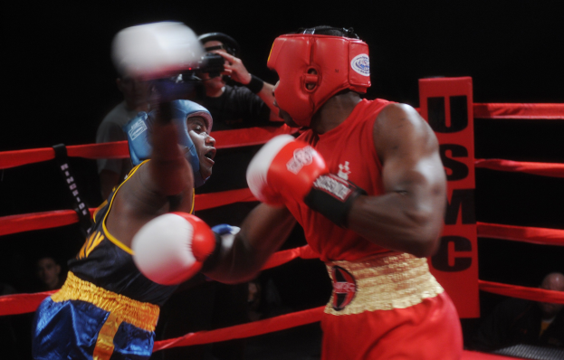 Zwei Boxer in einem Ring, die in einem Kampf gegeneinander antreten, mit einem Fotografen und Zuschauern im Hintergrund unter dramatischer Beleuchtung.