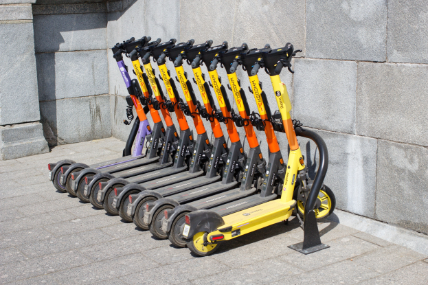 Eine Reihe von Elektro-Scootern ordentlich auf einem Gehweg mit einer Wand im Hintergrund geparkt.