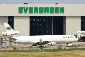 Ein Gebäude mit Text und einem Gitter, mit Flugzeugen auf dem Boden davor, einem Zaun, Treppen, Gras und dem Himmel.