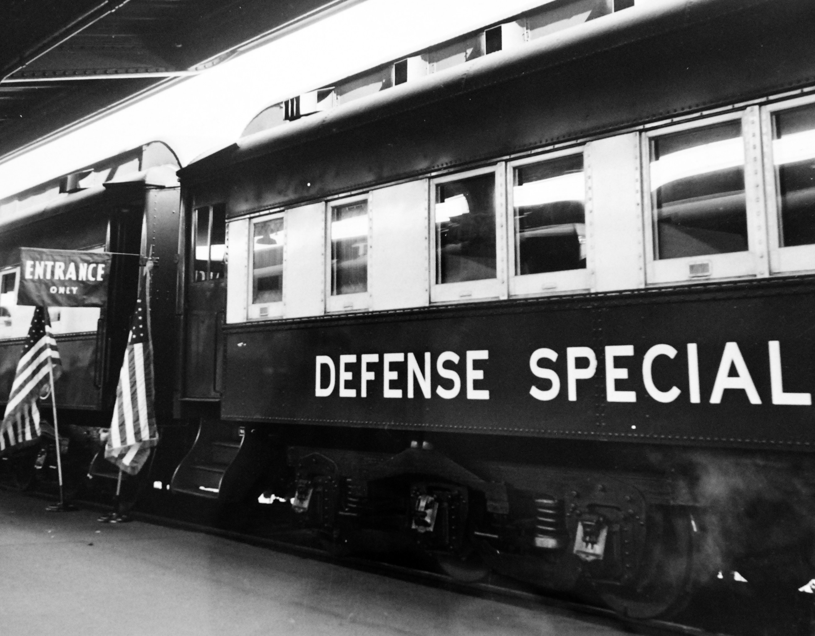 Schwarz-weiß-Foto eines Zuges mit der Aufschrift "Defense Special" auf den Gleisen mit zwei Fahnen links und einer Decke oben.