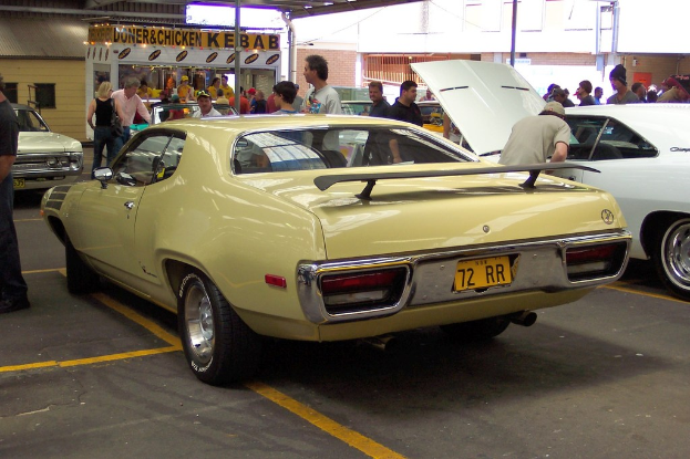 Ein Oldtimer steht auf einer Straße mit Menschen in der Nähe, ein Geschäft in der Mitte und Gebäude im Hintergrund.