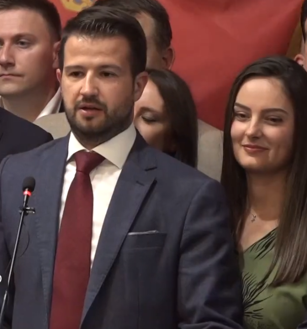 Ein Mann im Anzug und Krawatte steht an einem Rednerpult und hält eine Rede vor einer Menge mit einem Banner im Hintergrund, wahrscheinlich als Reaktion auf ein Regierungsverbot von Social Media.