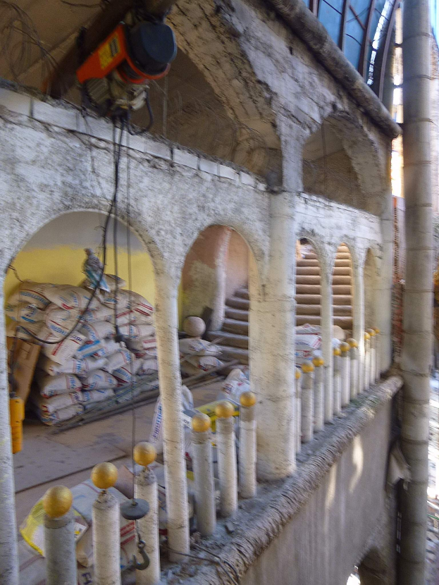 Altes Gebäude mit Bogengängen, Säulen, Treppen, Geländern, verstreuten Renovierungswerkzeugen und -materialien, mit einer Maschine und Drähten oben und Gegenständen auf der rechten Seite.