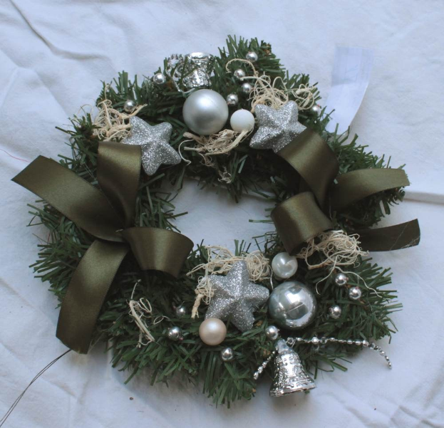 Ein festliches Weihnachtsgesteck mit Silberornamenten und Bändern auf einem weißen Tuch, mit bunten Kugeln, Sternen und anderen Verzierungen.