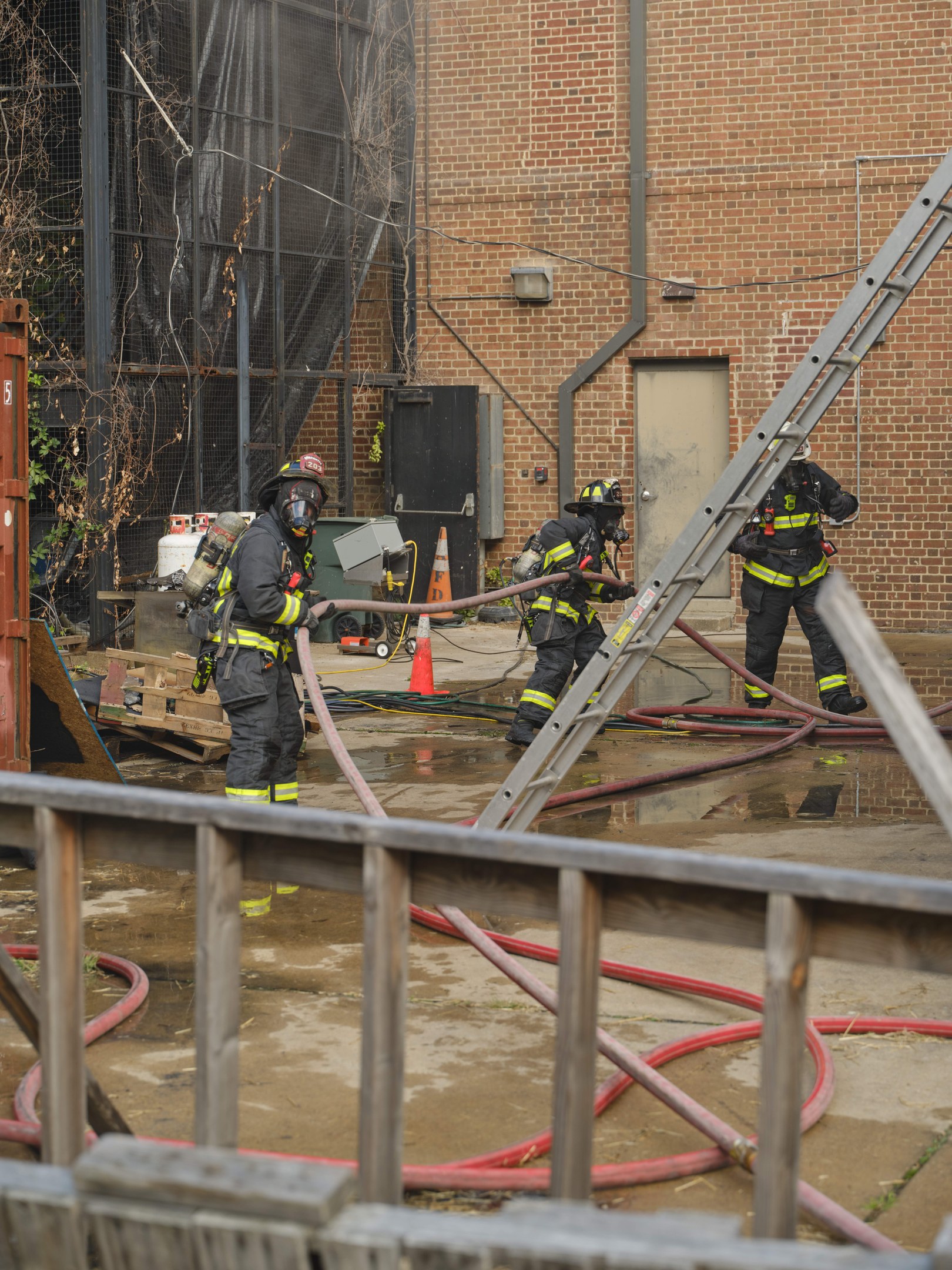 Feuerwehrleute in Helmen arbeiten daran, ein Gebäude Feuer zu löschen, mit Equipment und einem Zaun in der Nähe.