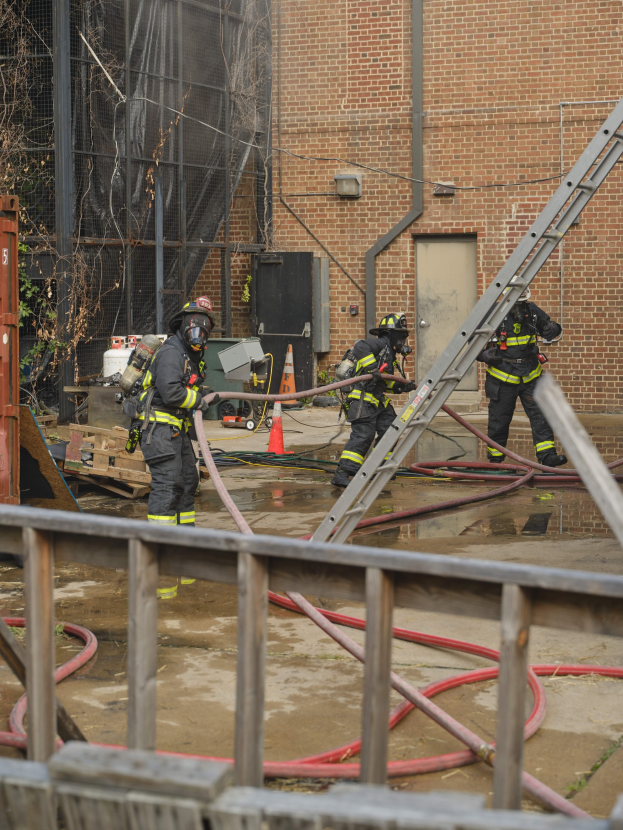 Feuerwehrleute in Helmen arbeiten daran, ein Gebäude Feuer zu löschen, mit Equipment und einem Zaun in der Nähe.