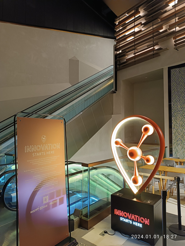 Großes Schild in der Mitte eines Gebäudes mit einer Treppe im Hintergrund, Tische und Stühle auf der rechten Seite und eine Tafel mit "Innovation Starts Here" auf der linken Seite, die auf die HSTP20 Expo hinweist.