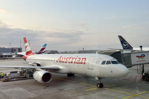 Austrian Airlines Airbus A330-300 auf dem Rollfeld am Frankfurter Flughafen mit Menschen, Fahrzeugen und Flughafen-Infrastruktur im Hintergrund unter einem klaren blauen Himmel.