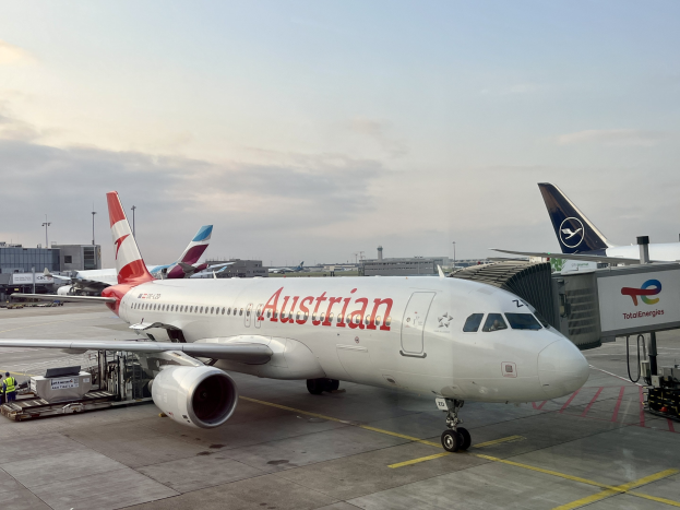 Austrian Airlines Airbus A330-300 auf dem Rollfeld am Frankfurter Flughafen mit Menschen, Fahrzeugen und Flughafen-Infrastruktur im Hintergrund unter einem klaren blauen Himmel.
