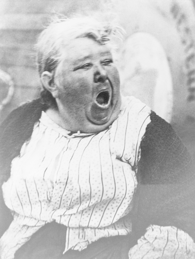 Ein altes Schwarz-Weiß-Foto einer schreienden Frau im Vordergrund, mit einer Wand und einigen Gegenständen im Hintergrund.