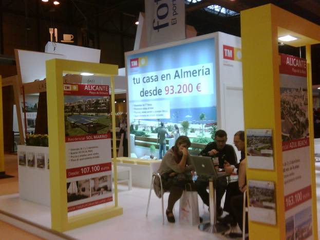 Eine Gruppe von Menschen sitzt um einen Tisch herum auf Stühlen und schaut auf einen Laptop, mit mehreren Flyern mit verschiedenen Werbeanzeigen daneben.