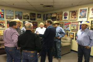 Eine Gruppe von Männern steht in einem Raum mit Sofas, Plakaten an den Wänden und Deckenlampen und ist in ein Gespräch vertieft.