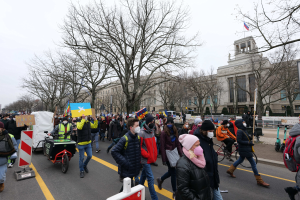Eine große Gruppe von Menschen marschiert in Washington, D.C. mit Schildern, Bannern und Fahrrädern unter einem klaren blauen Himmel.
