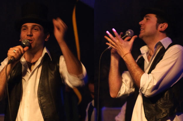 Eine Gruppe von Menschen mit zwei Personen im Vordergrund, die in Mikrofone singen.