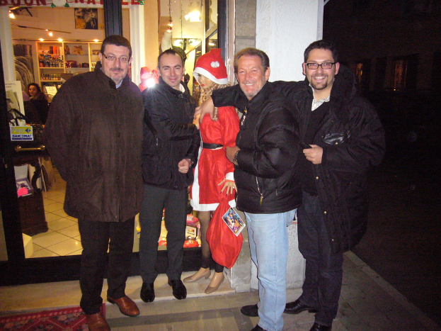 Menschen, die in einem Raum mit einem Santa Claus-Figur, Haustiergläsern, Vorhängen, Wandschmuck, Dekolichter und Papieren im Hintergrund stehen oder sitzen.