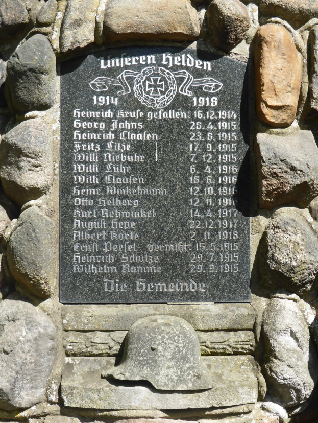 Steinmauer mit einer Gedenktafel mit Inschrift und einem Helm darauf, wahrscheinlich zur Erinnerung an den deutschen Militärdienst im Zweiten Weltkrieg.