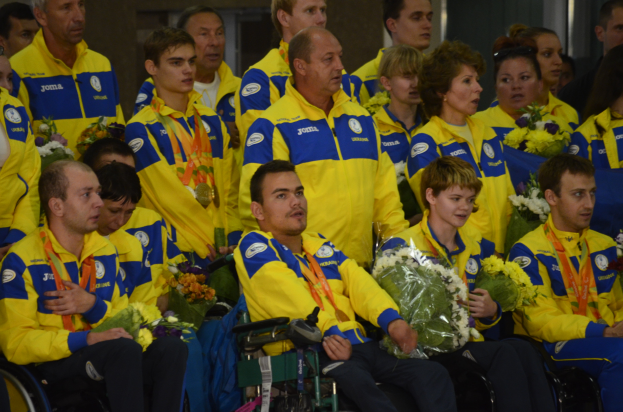 Eine Gruppe von Menschen im Rollstuhl, einige mit Blumensträußen und Medaillen, vor einer Wand im Hintergrund.
