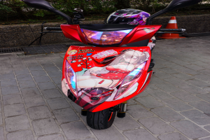 Ein oranger E-Scooter steht auf dem Straßenrand mit einem Helm darauf, mit einem Verkehrskegel, einer Wand und mehreren Bäumen im Hintergrund.