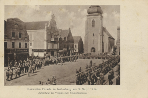 Ein Schwarz-Weiß-Foto eines Umzugs in Insterburg am 5. September 1914 mit vielen Menschen, Gebäuden im Hintergrund und Text unten auf dem Bild.