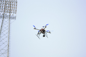 Eine Drohne fliegt durch die Luft mit einem Turm auf der linken Seite und einem klaren blauen Himmel im Hintergrund.