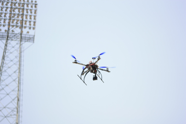 Eine Drohne fliegt durch die Luft mit einem Turm auf der linken Seite und einem klaren blauen Himmel im Hintergrund.