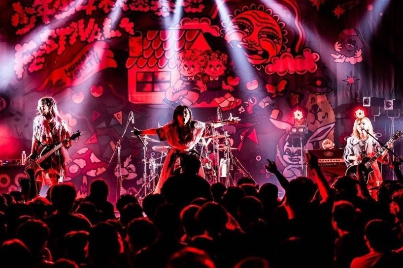 Ein Live-Auftritt der japanischen Rockband Korn auf der Bühne mit Musikern, die Gitarren spielen und singen, begleitet von Mikrofonen und Ständern, während das Publikum unten zuschaut.