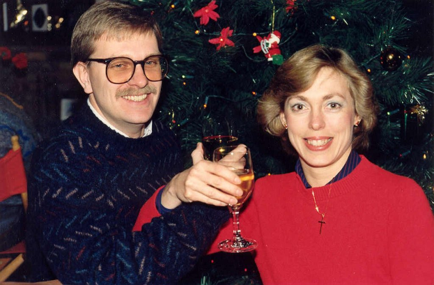 Ein Paar lächelt beim Halten von Weingläsern vor einem Weihnachtsbaum im Hintergrund.