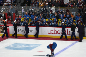 Eishockeyspieler auf dem Eis umgeben von Teamkollegen und Gegenspielern, mit Zuschauern im Hintergrund bei einem Spiel der Colorado Avalanche gegen die San Jose Sharks am 3/24/15.