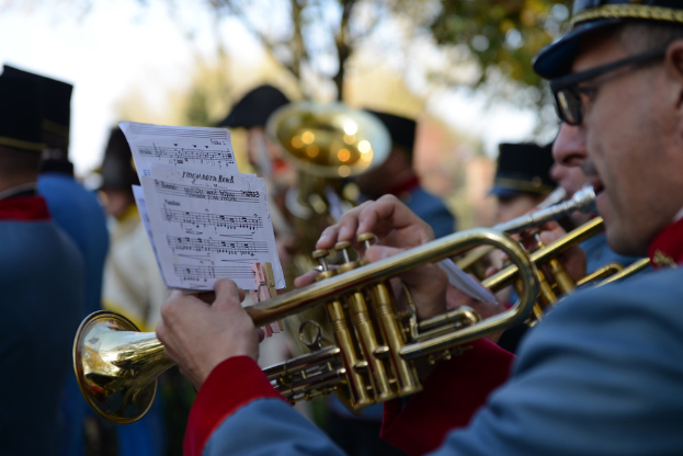 Eine Gruppe von Menschen in gleichen Kost├╝men, die Trompeten spielen, mit Noten vor sich und Bäumen im Hintergrund.