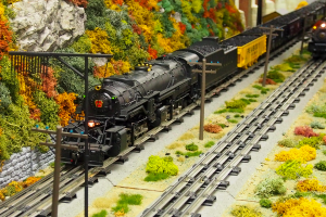 Zwei Spielzeughähne auf Schienen mit Pfählen und Pflanzen im Hintergrund.