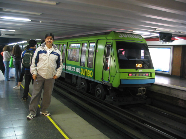 Ein Zug auf einem Bahnsteig mit Menschen auf der linken Seite und einem Dach oben im Bild.