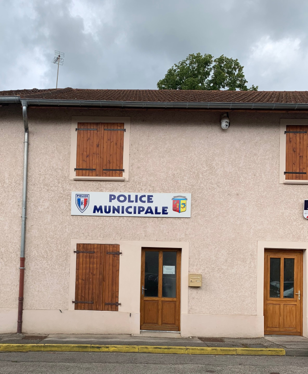 Polizeigebäude mit einem Schild, Fenstern, Türen, einer Namenskennung, einem Rohr, einem Baum und einem bewölkten Himmel im Hintergrund.