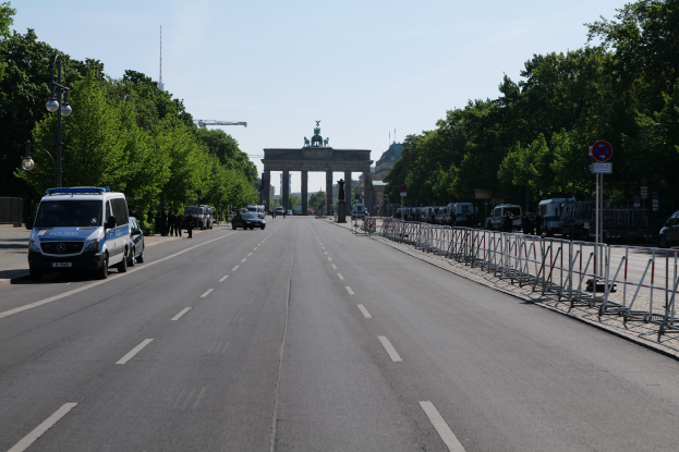 Ein Polizeiwagen steht am Straßenrand vor dem Reichstagsgebäude in Berlin, Deutschland, mit Barrieren, Schildern, Bäumen, Laternenmasten und einer bewölkten Himmelovisibilität.