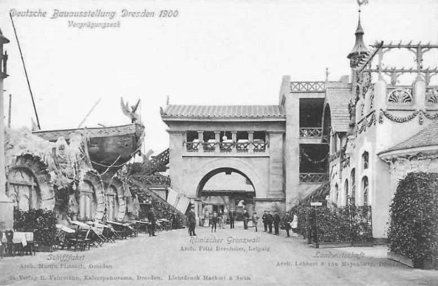 Schwarz-weiß-Foto von Menschen, die eine Straße in Dresden, Deutschland im Jahr 1900 entlanggehen, mit Gebäuden, Pflanzen und Stühlen, die die Straße säumen, und dem Himmel im Hintergrund sichtbar; Text ist oben und unten auf dem Bild vorhanden.