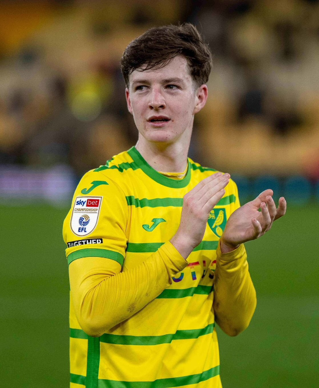 Ein junger Mann in einem gelb-grünen T-Shirt klatscht auf einem Fußballfeld, feiernd nach einem Tor mit unscharfem Hintergrund.